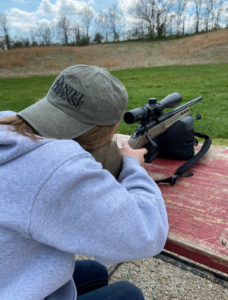 Female hunter practices with a rifle and riflescope on a picnic table